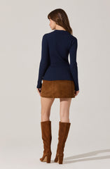 A woman is wearing a fitted navy blue ribbed sweater with a collar, a brown suede mini skirt, and tall brown suede boots with high block heels.
