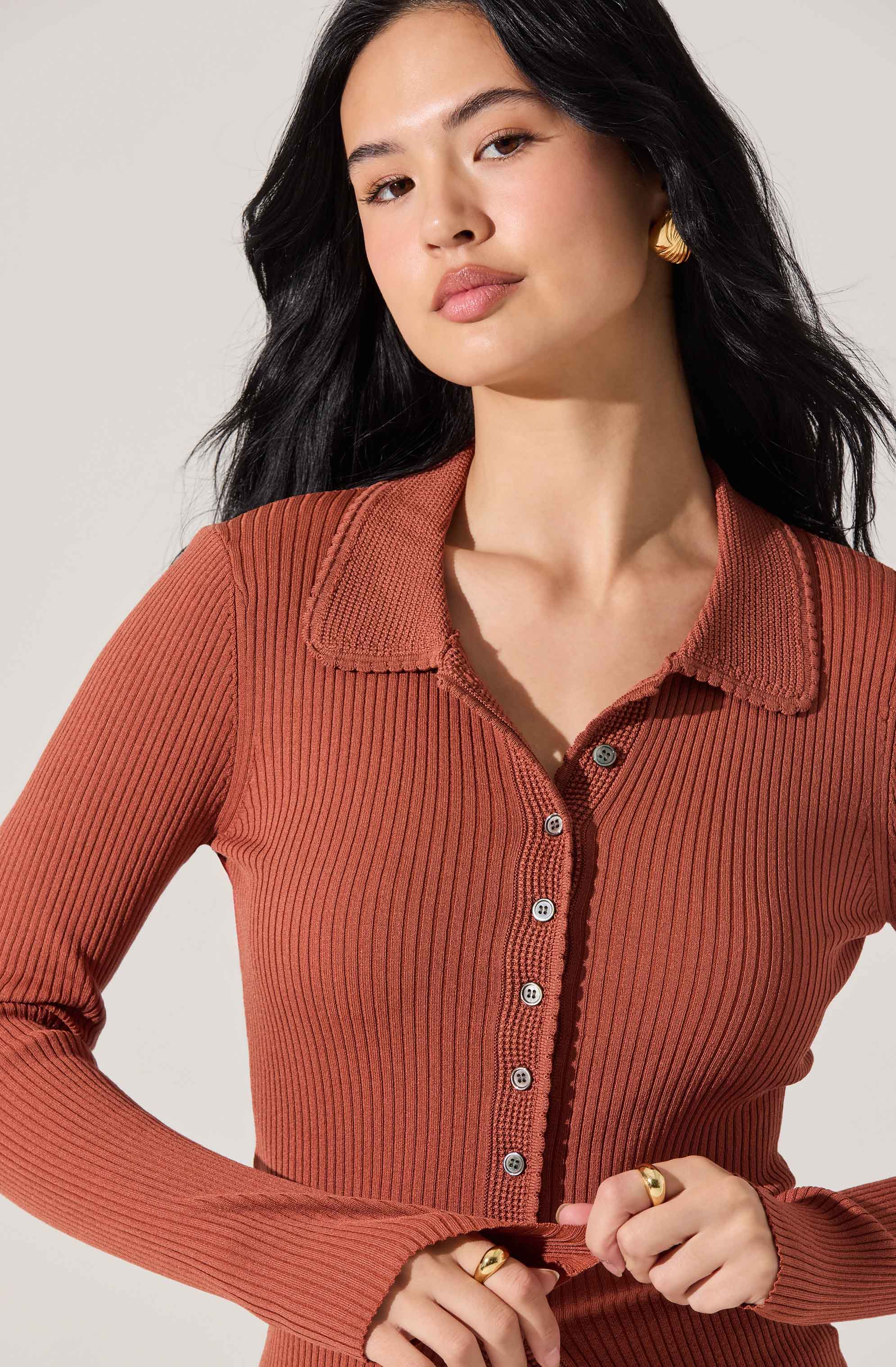 A woman is wearing a long-sleeved, ribbed, burnt orange shirt with a collared neckline. The shirt features a row of buttons down the front.
