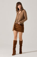A woman is wearing a light brown cardigan with a matching top underneath. She pairs this with a brown skirt and tall brown suede boots.