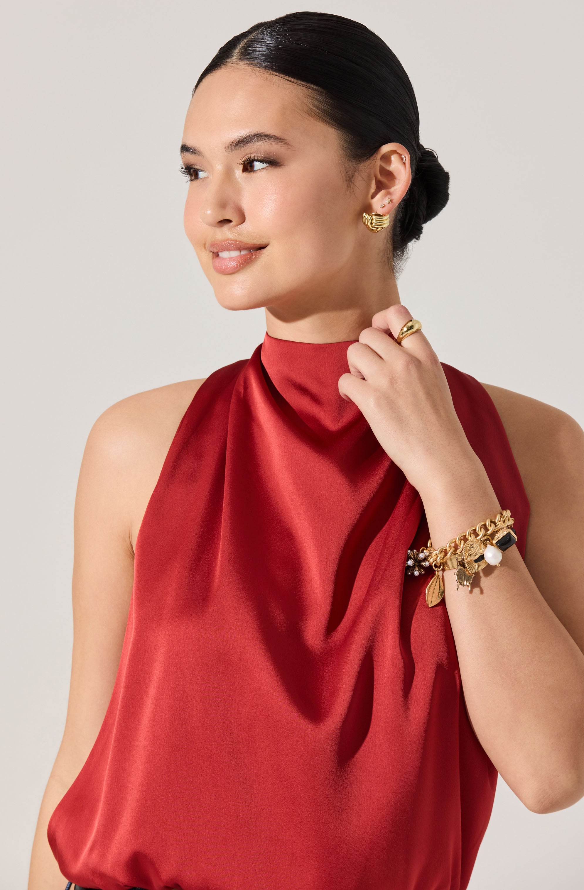 A woman wearing a sleeveless, high-neck, silky red blouse.