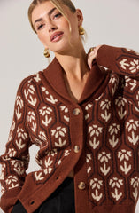 A woman wearing a brown, patterned cardigan with cream-colored leaf and geometric designs. The cardigan features a shawl collar and large buttons down the front.