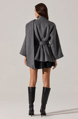 A woman is wearing a long, grey, wrap-style coat with wide sleeves that extend past her elbows, tied at the waist with a matching belt. She is also wearing a short black skirt and tall black leather boots with high heels.