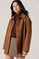 A woman is wearing a brown suede button-up coat with a classic collar, layered over a dark brown turtleneck sweater. She pairs this with a beige and brown houndstooth patterned skirt.