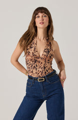 A woman is wearing a sleeveless, V-neck top with a tan background and a black and dark brown leopard print pattern. She pairs it with high-waisted, dark blue jeans with a black belt that has a gold buckle.