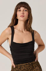 The woman is wearing a fitted black sleeveless top with thick straps and gathers across the bust, paired with high-waisted leopard print pants. She is also wearing gold earrings.