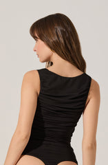 A woman is wearing a sleeveless, fitted black top with ruched detailing across the back.