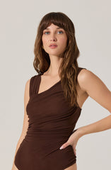 A woman is wearing a sleeveless, dark brown top with a draped, ruched design that gathers around the waist and chest. The top has wide shoulder straps and a V-shaped neckline.