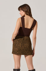 A woman is wearing a sleeveless, dark brown top with wide shoulder straps and a deep scoop back, paired with a high-waisted, leopard print mini skirt.