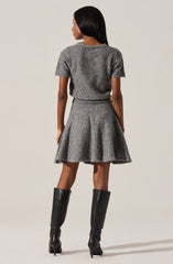 A woman is wearing a matching grey knit short-sleeve sweater and a flared skirt, both made of a soft, textured material. The sweater has a decorative trim around the neckline. She is also wearing tall black leather knee-high boots with high heels.
