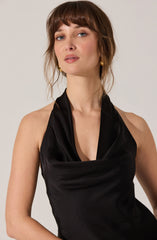 A woman is wearing a sleeveless, black satin dress with a cowl neckline.