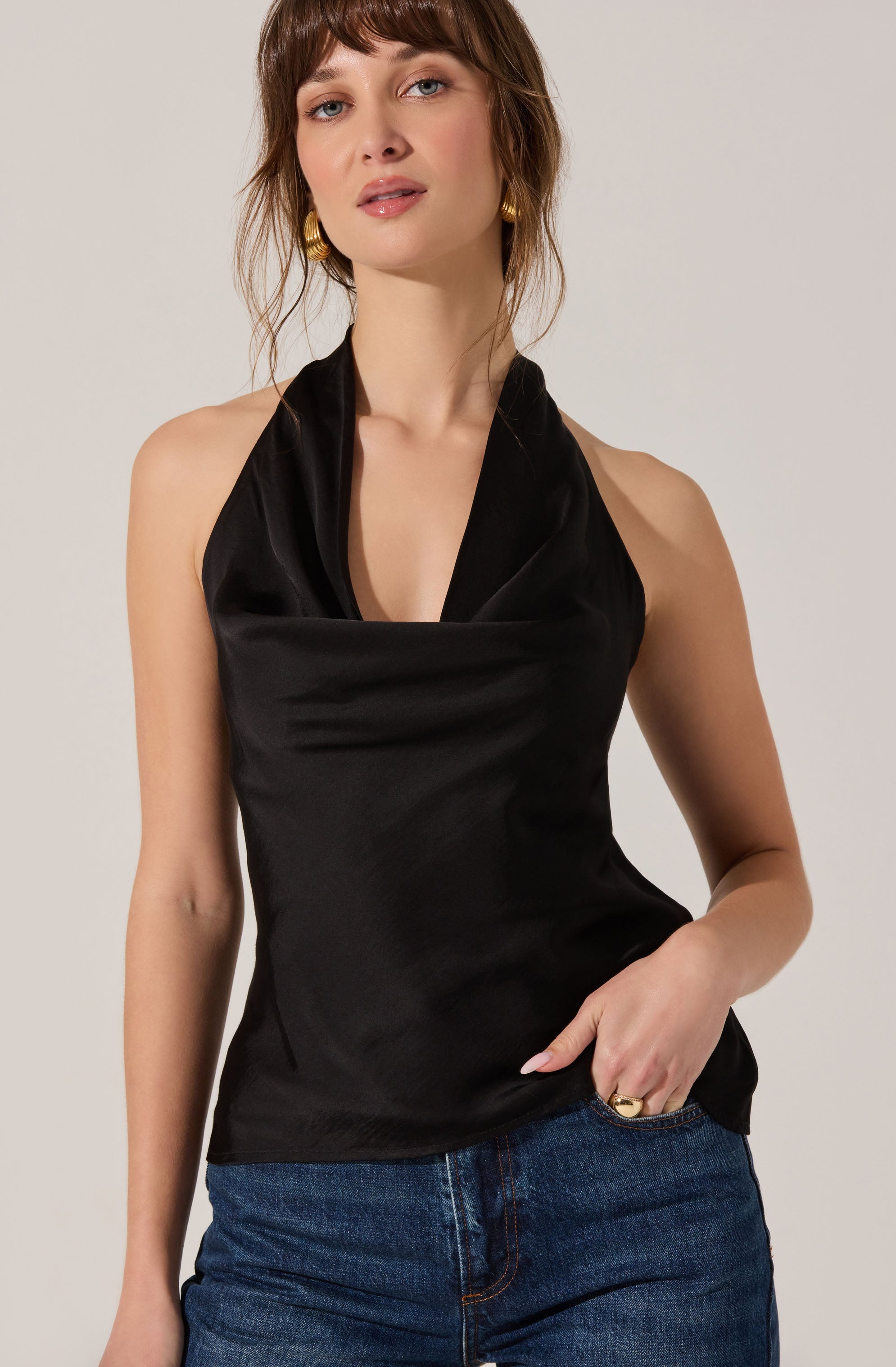 A woman is wearing a sleeveless black satin top with a draped cowl neckline that creates a soft fold at the front.