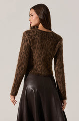 A woman is wearing a long-sleeved, fuzzy brown sweater with a subtle leopard print pattern, paired with a high-waisted, dark leather A-line skirt.