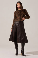 A woman is wearing a long-sleeved, brown fuzzy cardigan with a leopard print pattern and buttons down the front. She pairs it with a high-waisted, A-line leather skirt in dark brown or black that falls below the knees. She completes the outfit with tall, black leather high-heeled boots.