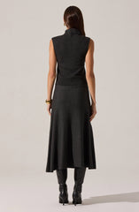A woman is wearing a sleeveless, high-neck, dark gray or charcoal top made of a textured, woven fabric. She has paired it with a matching long, flowing A-line skirt that reaches just above her ankles. She is also wearing black, high-heeled knee-high boots.