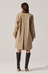 A woman is wearing a beige trench coat with a brown collar. The coat has long sleeves with buttoned straps near the cuffs, and it extends down to her knees. She is also wearing tall, black high-heeled leather boots.