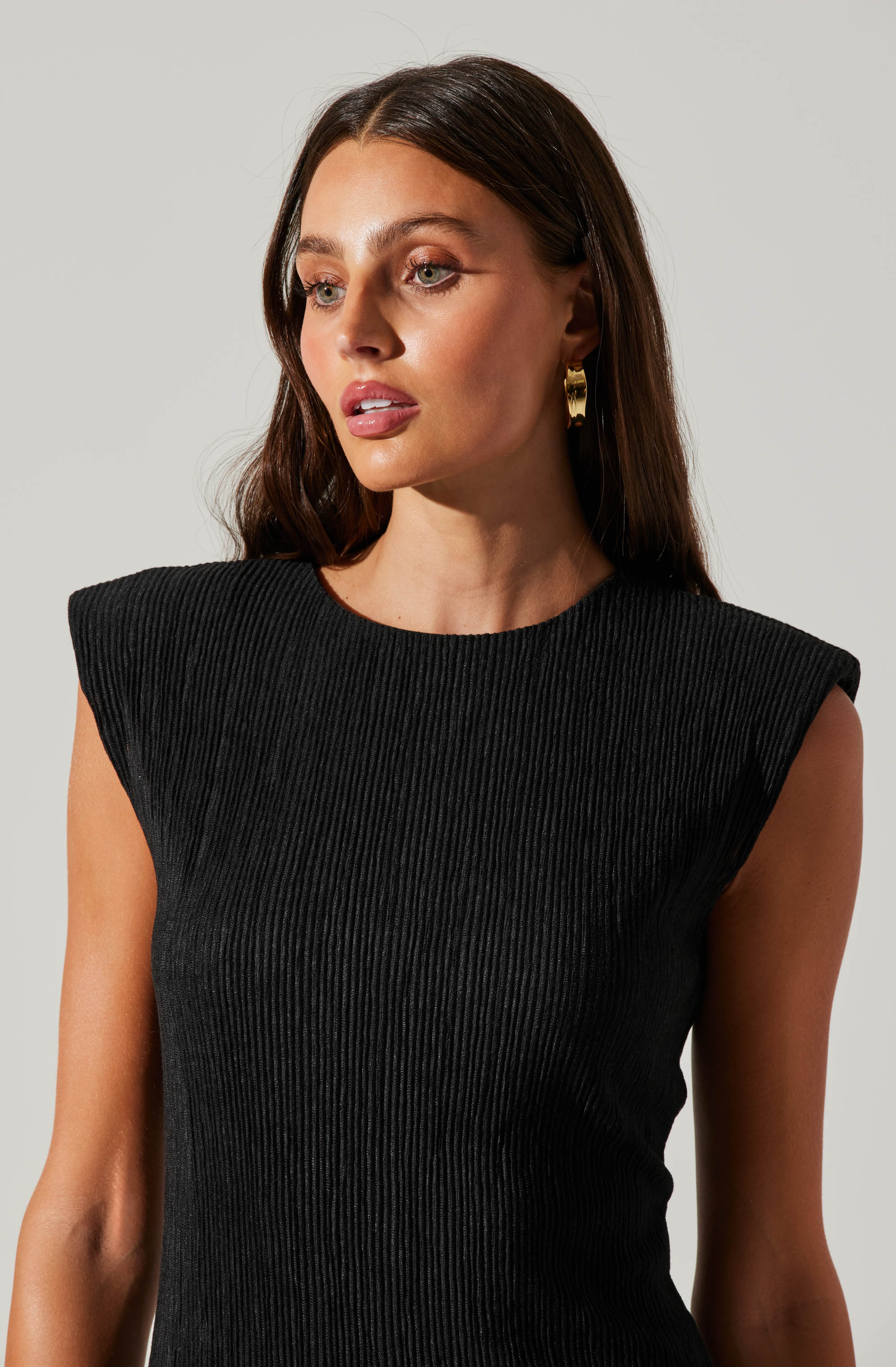 A woman wearing a black, sleeveless, ribbed top with structured, padded shoulders.