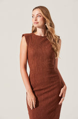 A woman wearing a sleeveless, form-fitting dress in a rust or burnt orange color with a textured, ribbed fabric. The dress features padded shoulders and a round neckline.