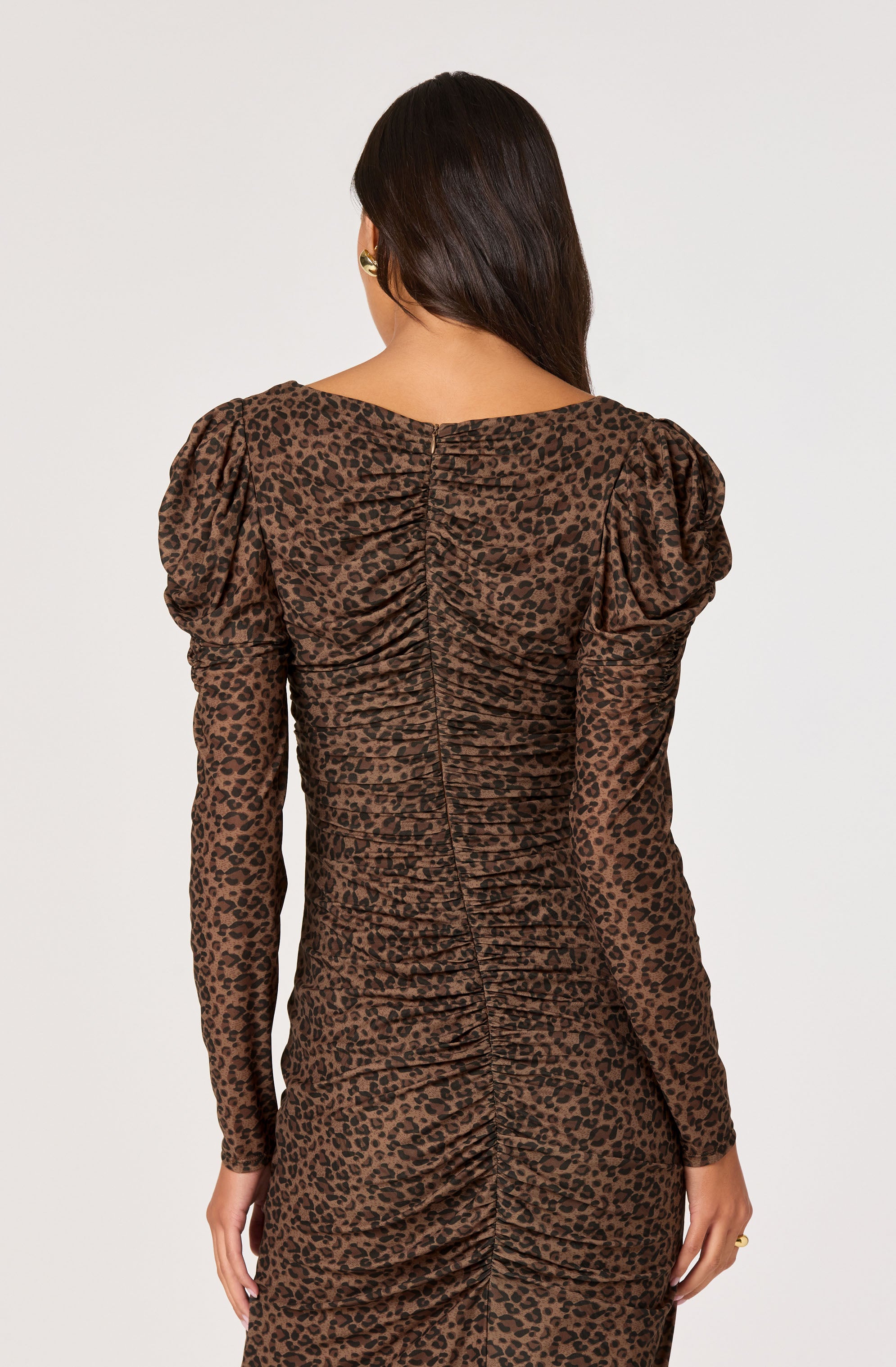 A woman is wearing a fitted, long-sleeved dress with a leopard print pattern. The dress features shoulder puffs and ruched detailing down the back.