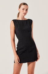 A woman is wearing a sleeveless, knee-length black dress with a fitted silhouette. The dress has a subtle textured pattern and a round neckline.