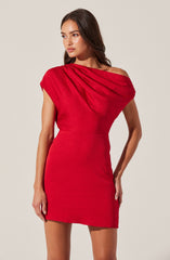 A woman is wearing a short, fitted red dress with an asymmetric neckline. The dress features pleated detailing on the right shoulder, creating a draped effect. The fabric appears to be smooth and slightly stretchy.
