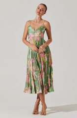 A woman is wearing a sleeveless, V-neck, spaghetti strap dress with a vibrant, multicolored floral pattern. The dress features a fitted bodice and a pleated skirt that falls below the knees. She is also wearing strappy high-heeled sandals.