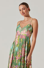 A woman is wearing a sleeveless, ankle-length dress with thin spaghetti straps. The dress features a vibrant floral pattern with shades of pink, purple, green, and blue, and has a fitted bodice with a slightly gathered, flowing skirt.