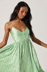 A woman is wearing a sleeveless, light green dress with thin spaghetti straps. The dress features a ruched bust and a high waistline, with a pleated skirt that has white polka dots throughout.