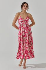 A woman is wearing a sleeveless, ankle-length dress with spaghetti straps. The dress features a fitted bodice and a gathered waist, with a vibrant pink and beige floral pattern throughout. She is also wearing a pair of light-colored, open-toe heels.