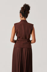 The woman is wearing a sleeveless, brown vest with a collar and a matching waist belt. She is also wearing a long, pleated skirt in a matching brown color.