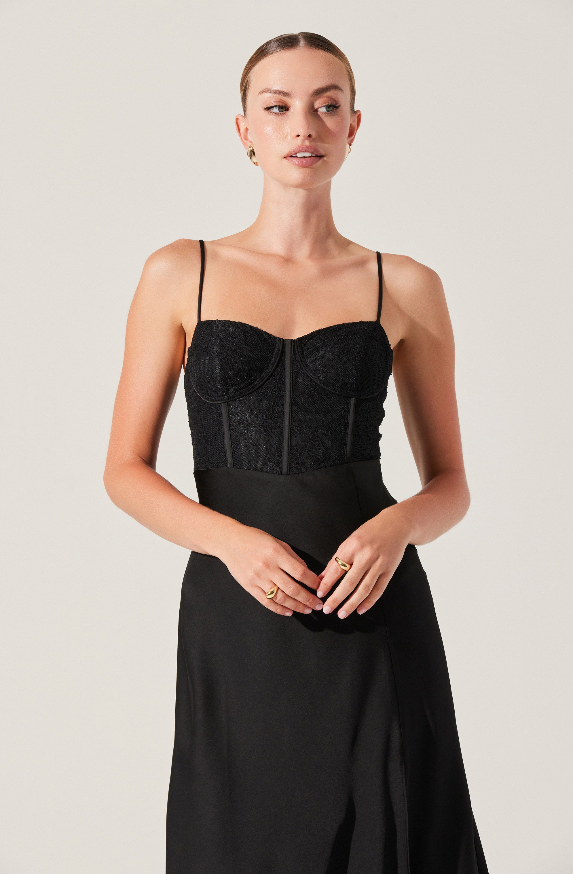 The woman is wearing a black sleeveless top with thin spaghetti straps. The top has a fitted bodice with decorative lines and a front zipper, featuring a textured fabric with a subtle floral pattern. She pairs it with a high-waisted black skirt that has a smooth texture and a slight slit in the front.