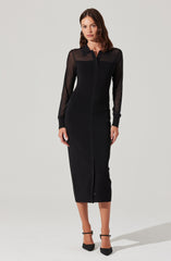 A woman is wearing a black, long-sleeved, button-up dress with sheer sleeves and a structured collar. The dress is fitted and extends to mid-calf length with a front zipper. She is also wearing black ankle-strap pointed-toe heels.