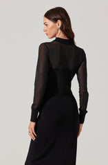 A woman is wearing a black dress with sheer long sleeves and a fitted silhouette. The dress appears to have a high neckline and is made of a smooth, matte fabric. The sheer sleeves add a delicate and elegant touch to the overall look.