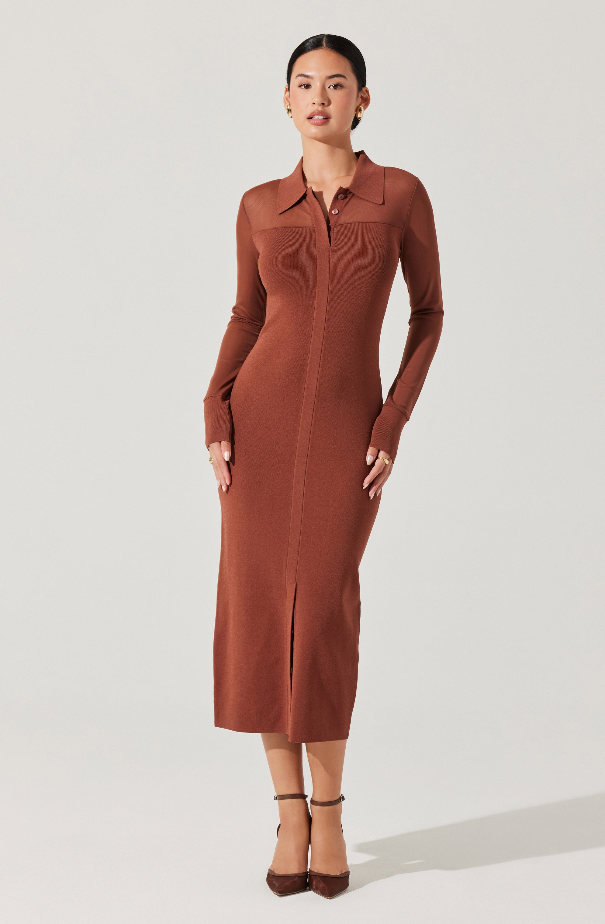 A woman is wearing a long, fitted dress in a warm, earthy brown color. The dress has a collared neckline, a concealed front zipper, and long sleeves. It features a front slit at the hem, adding a touch of elegance. The fabric appears to be smooth and slightly stretchable.