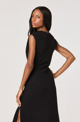 A woman is wearing a sleeveless black dress that is fitted at the waist and has a slit on the side. The dress appears to be made of a smooth, slightly textured fabric.