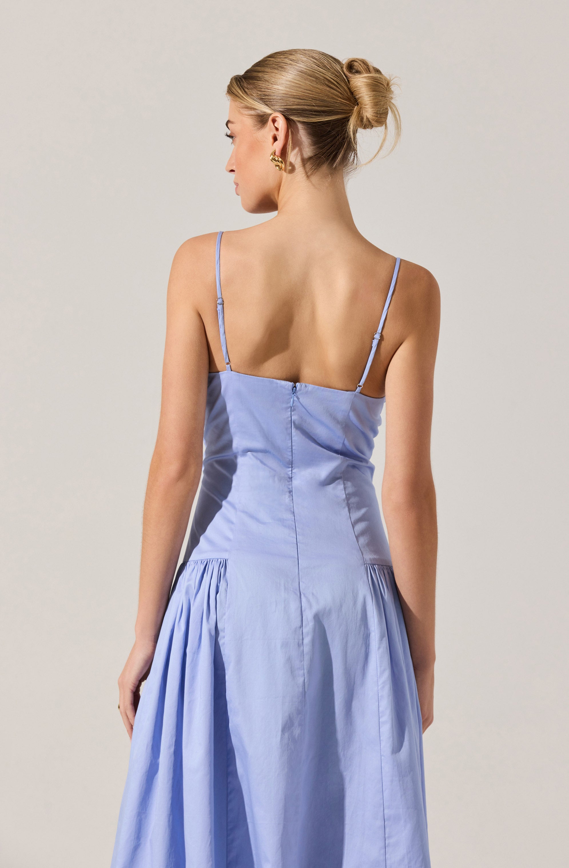 The woman is wearing a light blue, sleeveless dress with thin spaghetti straps. The dress features a fitted bodice with a zipper closure at the back and a full, gathered skirt.
