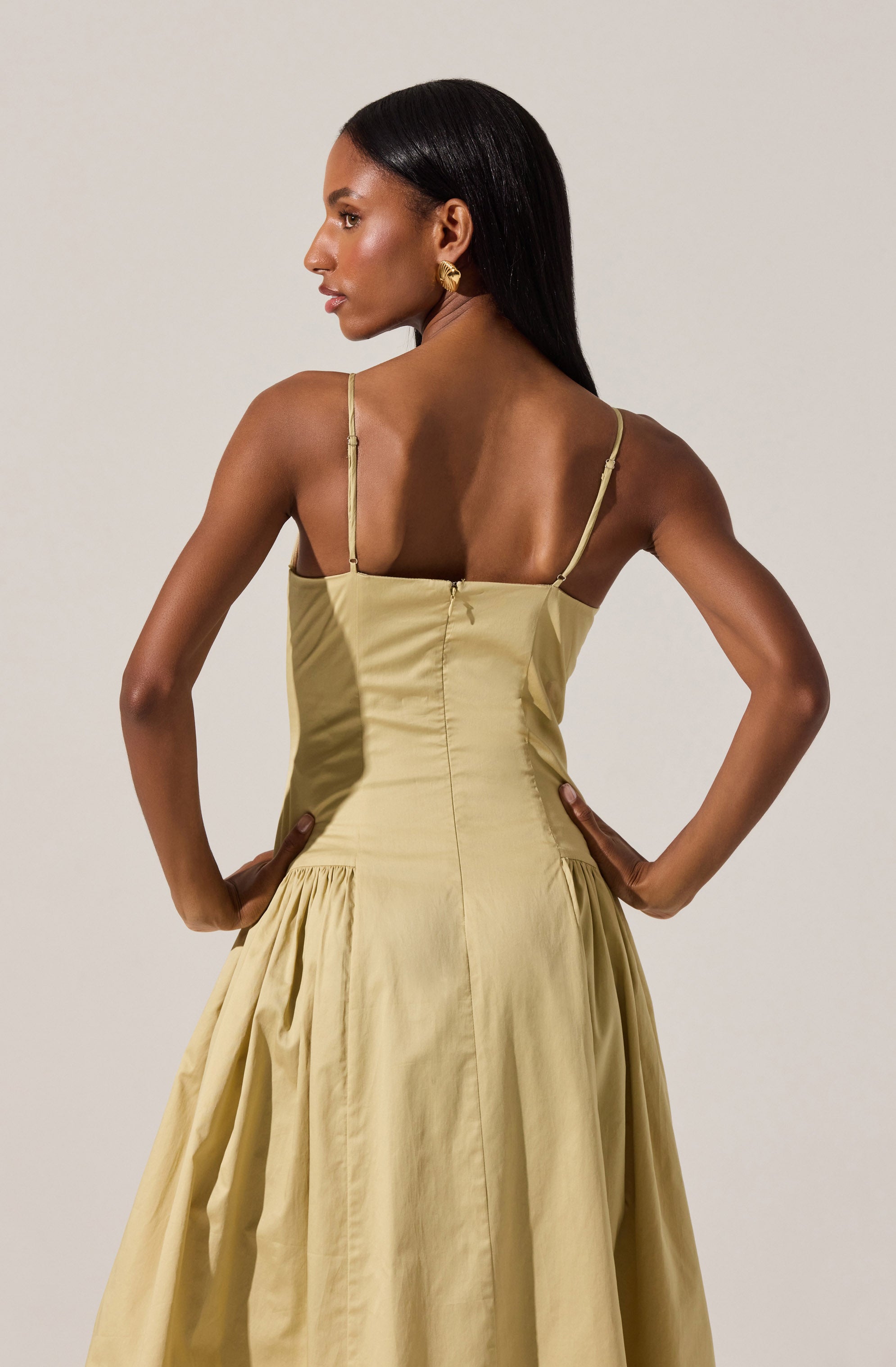 The dress is a sleeveless, light yellow, satin-like gown with thin adjustable spaghetti straps, a fitted bodice with visible side seams, and a full, gathered skirt that starts at the waist.
