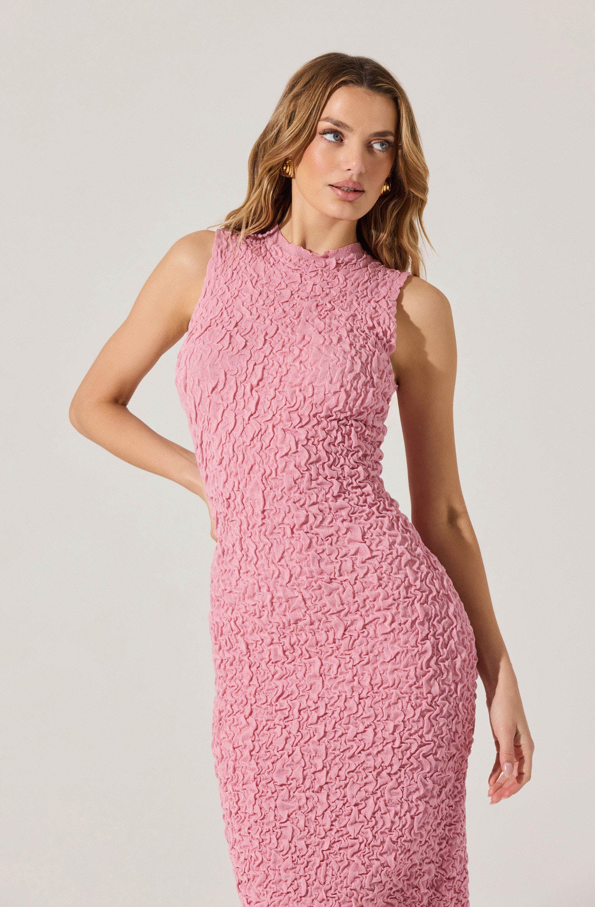 A woman is wearing a sleeveless, fitted pink dress made of textured fabric with a crinkled, ruffled appearance.