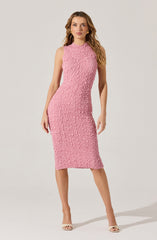 A woman is wearing a sleeveless, knee-length pink dress with a textured, crinkled fabric pattern. She has on beige open-toe heels and gold hoop earrings.