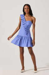 A woman is wearing a light blue dress with a one-shoulder design. The right shoulder features a ruffled strap that runs diagonally across the front of the dress. The dress has a fitted bodice and a gathered, ruffled skirt that falls above the knees. She is also wearing white heels.