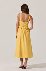 A woman is wearing a sleeveless, yellow dress with wide straps, fitted at the waist, and a full, mid-calf length skirt. She is also wearing black high-heeled sandals.