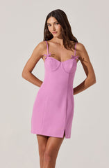 A woman is wearing a sleeveless, light purple dress with thin spaghetti straps. The dress features decorative bows at the shoulders, a fitted bodice with visible seam details, and a small slit on the front left side. The fabric appears smooth and slightly stretchy.