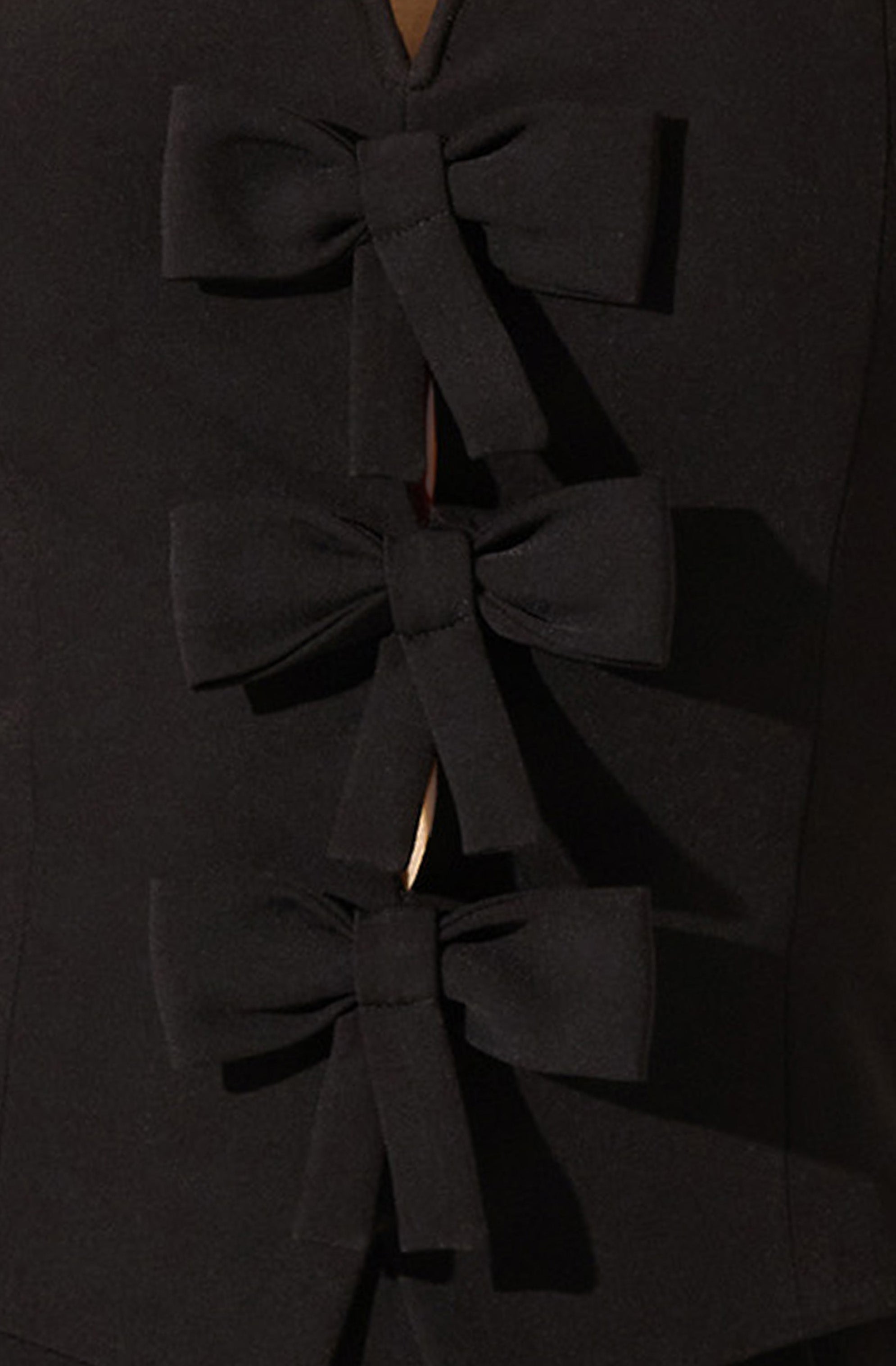 The image shows a black garment with three decorative fabric bows aligned vertically. Each bow is made of the same black fabric and is tied in a classic bow shape with loops and tails. The material appears to be sturdy and possibly has a matte finish. The overall look is elegant and sophisticated.