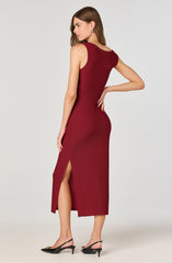 A woman is wearing a sleeveless, ankle-length, deep red dress with a side slit. The dress has a fitted silhouette and features a round neckline. She is pairing the outfit with black high-heeled sandals with ankle straps.