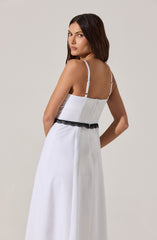 A woman is wearing a long, white dress with thin white shoulder straps. The dress features a fitted shirred bodice and a black lace trim around the waist.