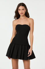 A woman is wearing a strapless black dress with a fitted bodice and a pleated, flared skirt.