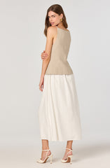 A woman is wearing a sleeveless beige top with a fitted bodice and a subtle textured pattern. She pairs it with a long, flowing white skirt that reaches her ankles. She completes her outfit with cream-colored high-heeled sandals that have ankle straps.
