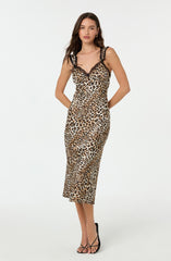 A woman is wearing a sleeveless, form-fitting dress with a leopard print pattern. The dress features black lace trim along the neckline and on the shoulder straps. She pairs the dress with black high-heeled sandals.