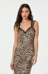 A woman is wearing a sleeveless, leopard print slip dress with black lace trim along the neckline and shoulder straps. The dress features a fitted silhouette with a pattern of black, brown, and beige spots resembling a leopard's coat.