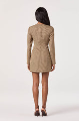 The woman is wearing a fitted, long-sleeve, camel-colored mini dress with a subtle pinstripe pattern. She is also wearing a pair of high-heeled shoes.