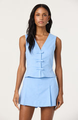 A woman is wearing a sleeveless, light blue, fitted top with a V-neckline and decorative horizontal ties down the front, paired with a matching light blue mini skirt featuring pleats.